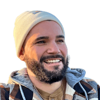 a bearded man with a beanie smiles in front of a black background